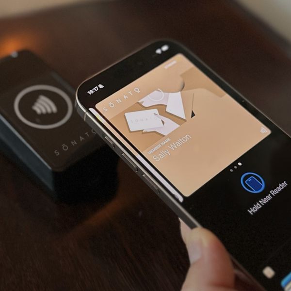 An iPhone with the Sonato membership pass in Apple Wallet, held to the reader at a club door